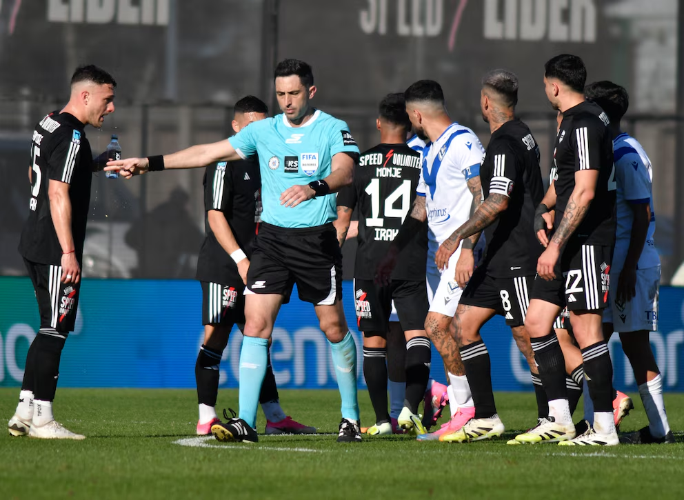 Nazareno Arasa rodeado de futbolistas tras anular el gol de Vélez en el partido contra Riestra.