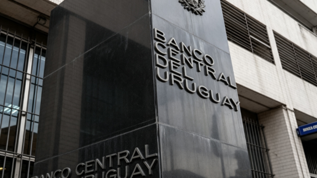 Monedas de peso uruguayo y billetes de dólar estadounidense sobre una superficie plana.