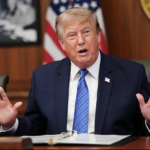 Donald Trump hablando en una conferencia flanqueado por pantallas con gráficos de inteligencia artificial.