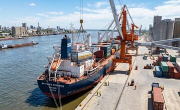 Barco de carga en un puerto agroindustrial argentino realizando la carga de granos y subproductos para exportación.