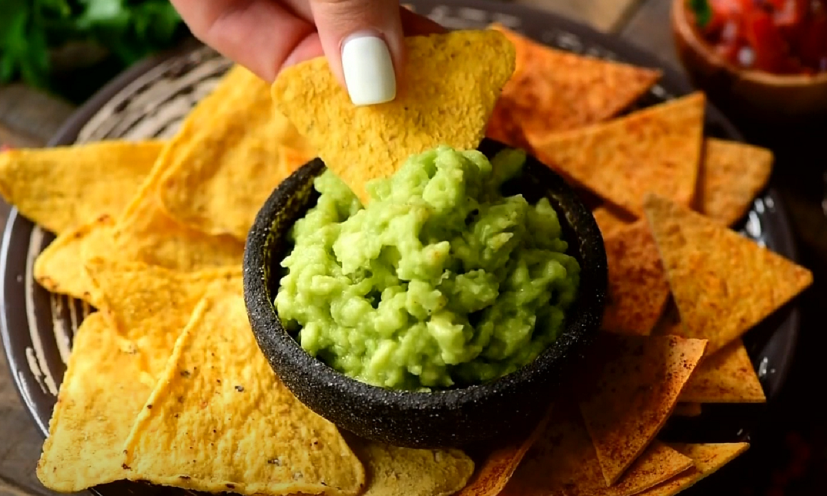 Recipiente de piedra con guacamole fresco preparado junto a nachos de maíz.