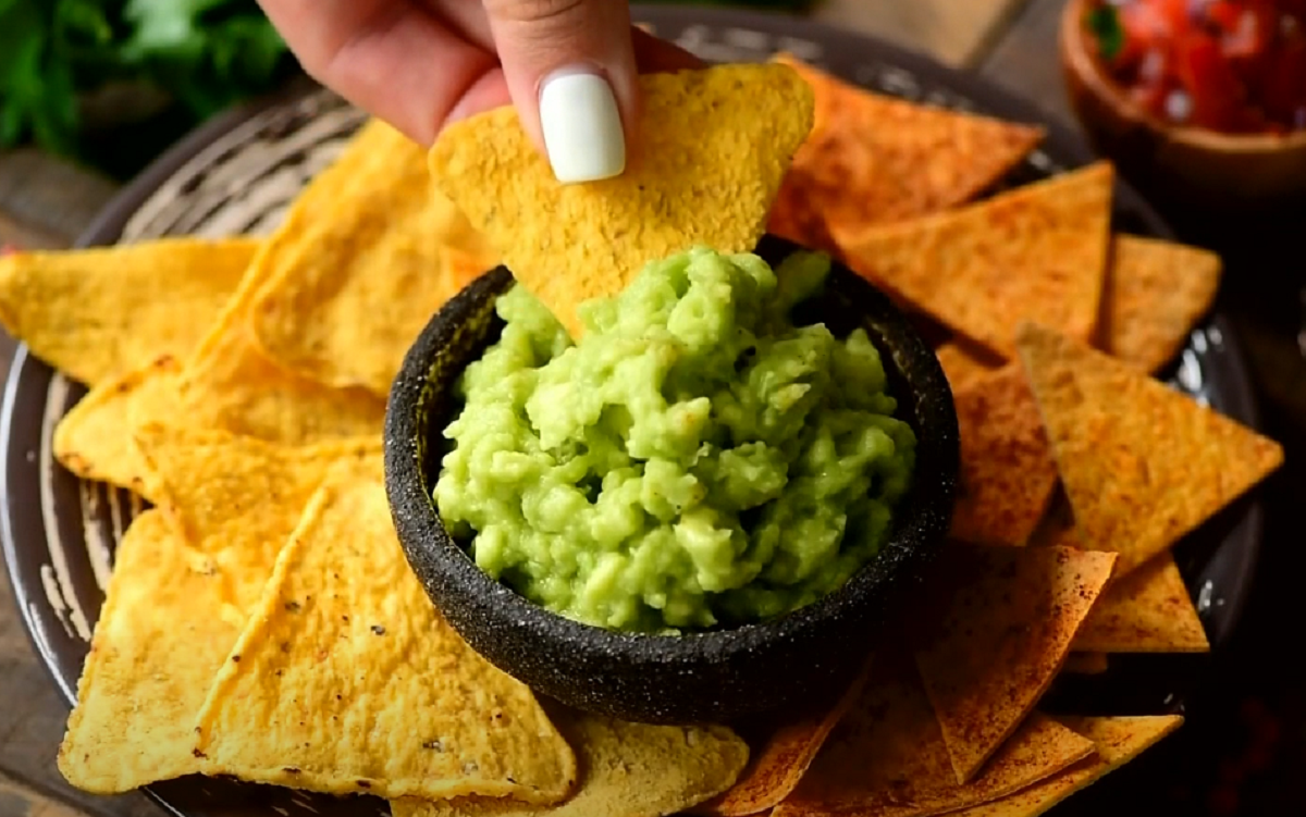 Recipiente de piedra con guacamole fresco preparado junto a nachos de maíz.