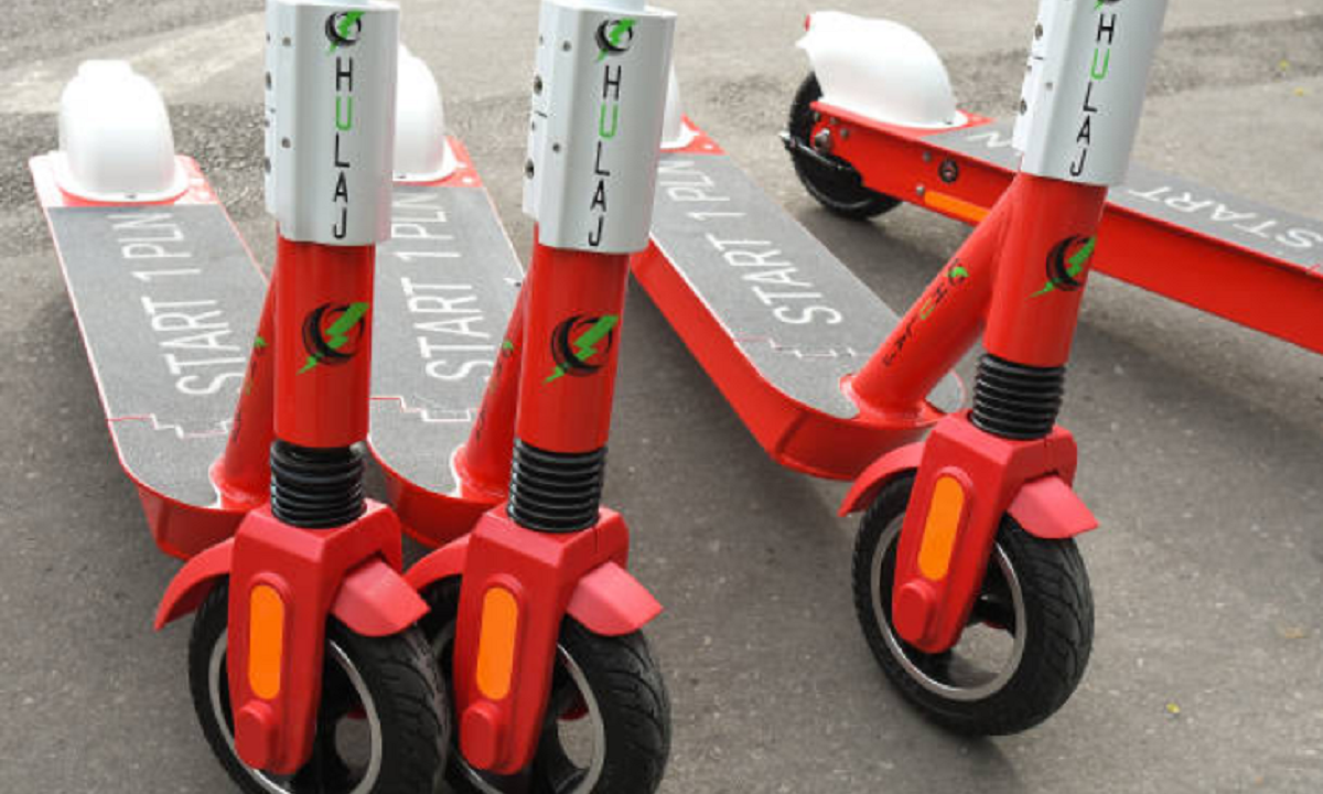 Monopatín eléctrico circulando por una avenida con casco y chaleco reflectivo exigidos por normativa.