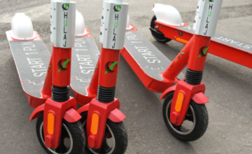 Monopatín eléctrico circulando por una avenida con casco y chaleco reflectivo exigidos por normativa.