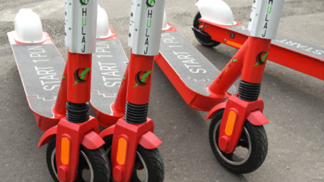 Monopatín eléctrico circulando por una avenida con casco y chaleco reflectivo exigidos por normativa.