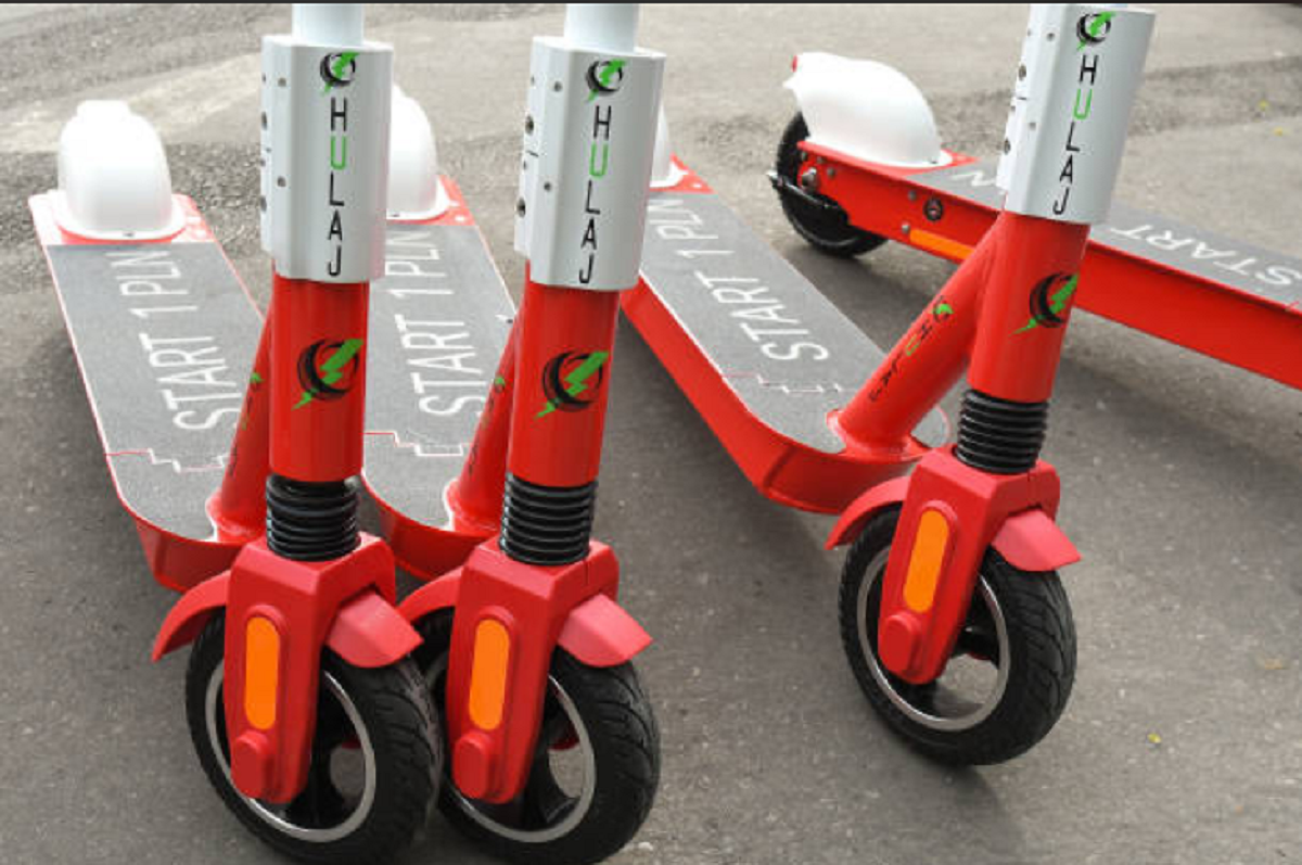 Monopatín eléctrico circulando por una avenida con casco y chaleco reflectivo exigidos por normativa.