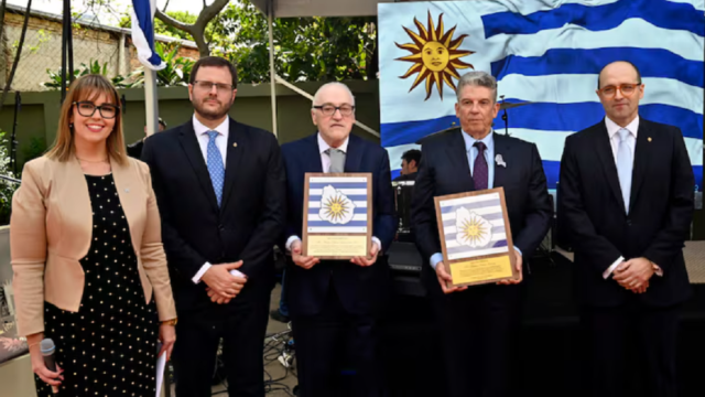 Autoridades y homenajeados posan con la bandera de Uruguay durante la recepción.