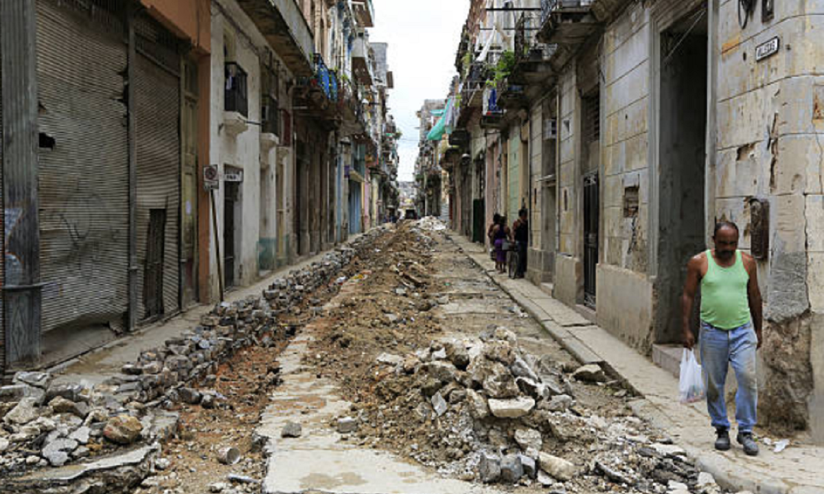 Persona mayor caminando frente a fachadas deterioradas en una calle de La Habana.