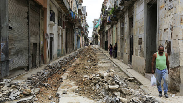 Persona mayor caminando frente a fachadas deterioradas en una calle de La Habana.