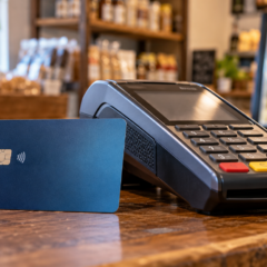 Tarjeta de débito bancaria apoyada sobre un mostrador junto a un dispositivo pos de cobro electrónico.