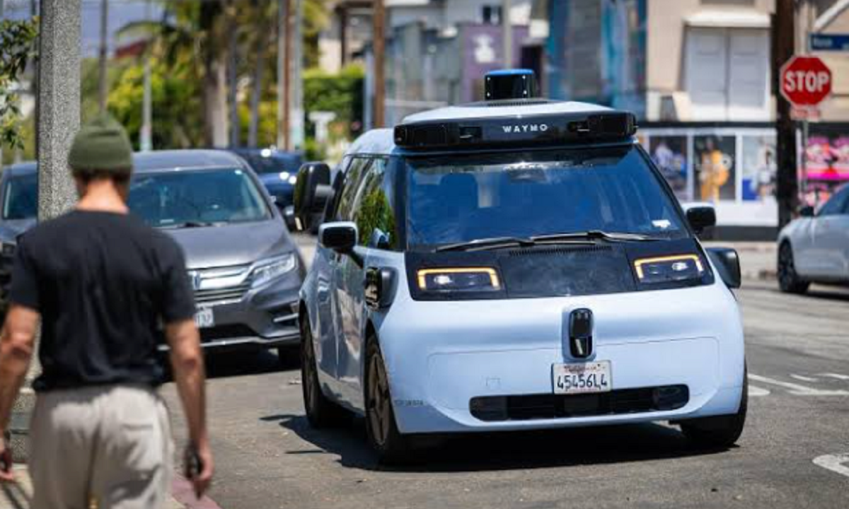 Vehículo autónomo de Waymo transitando por una calle urbana junto a un peatón.