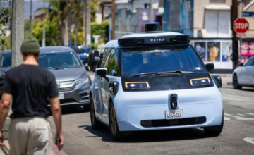 Vehículo autónomo de Waymo transitando por una calle urbana junto a un peatón.