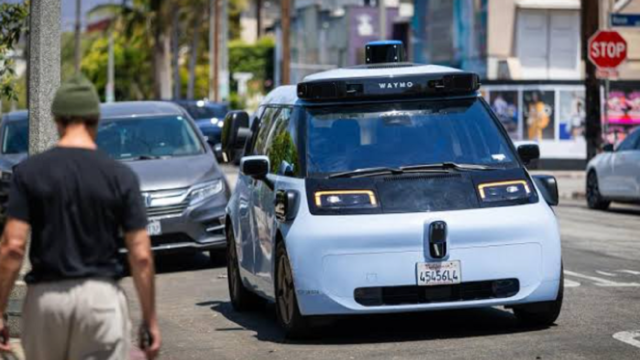 Vehículo autónomo de Waymo transitando por una calle urbana junto a un peatón.