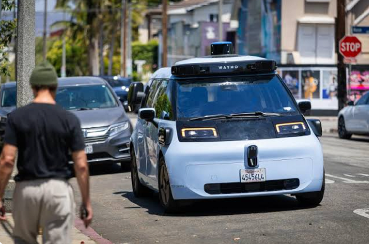 Vehículo autónomo de Waymo transitando por una calle urbana junto a un peatón.