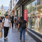 Personas caminando frente a vidrieras con carteles de descuentos en una peatonal comercial.