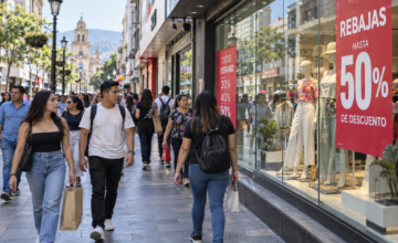Personas caminando frente a vidrieras con carteles de descuentos en una peatonal comercial.