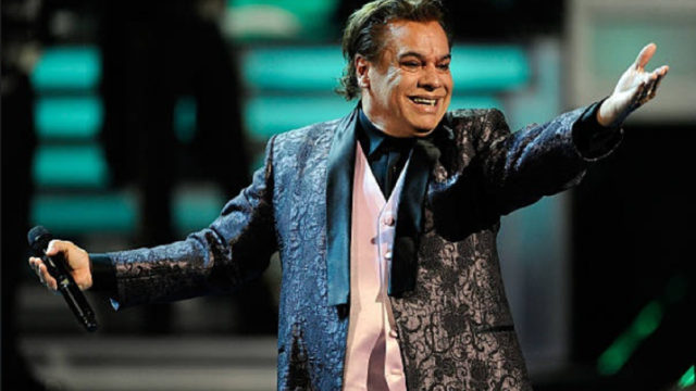 Juan Gabriel sonriendo en el escenario con traje morado.