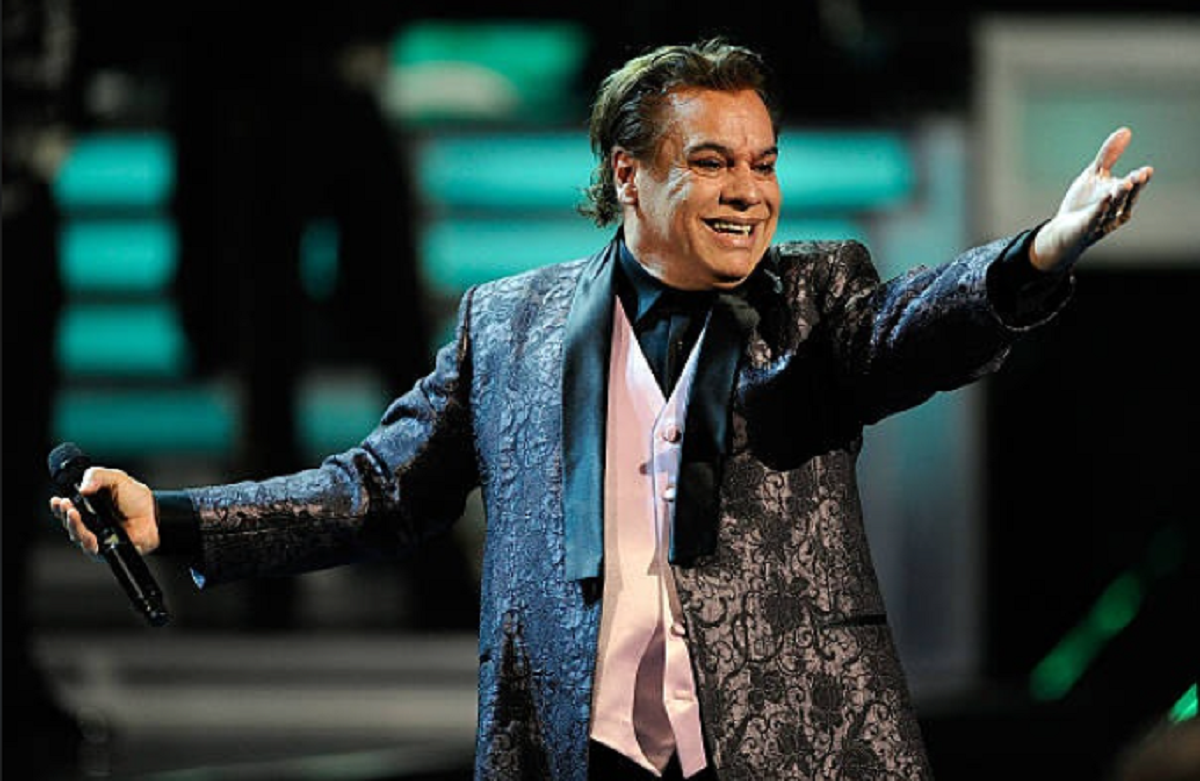 Juan Gabriel sonriendo en el escenario con traje morado.